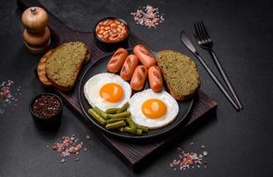 Tasty English breakfast of fried eggs, beans, asparagus, sausages with spices and herbs photo
