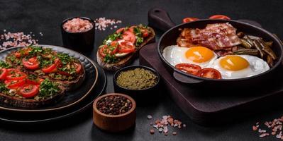 Tasty breakfast consists of eggs, bacon, beans, tomatoes, with spices and herbs photo