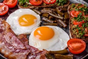Tasty breakfast consists of eggs, bacon, beans, tomatoes, with spices and herbs photo