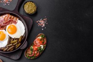 Tasty breakfast consists of eggs, bacon, beans, tomatoes, with spices and herbs photo