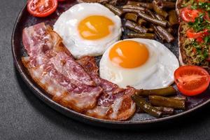 Tasty breakfast consists of eggs, bacon, beans, tomatoes, with spices and herbs photo