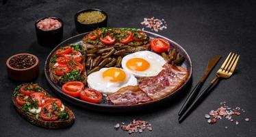 Tasty breakfast consists of eggs, bacon, beans, tomatoes, with spices and herbs photo