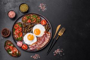 Tasty breakfast consists of eggs, bacon, beans, tomatoes, with spices and herbs photo