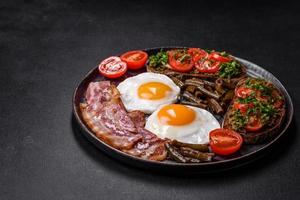 Tasty breakfast consists of eggs, bacon, beans, tomatoes, with spices and herbs photo