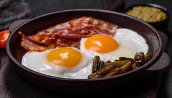 Tasty breakfast consists of eggs, bacon, beans, tomatoes, with spices and herbs photo