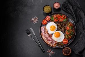 Tasty breakfast consists of eggs, bacon, beans, tomatoes, with spices and herbs photo