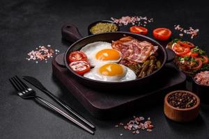 Tasty breakfast consists of eggs, bacon, beans, tomatoes, with spices and herbs photo
