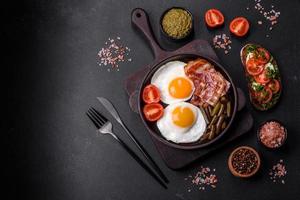 Tasty breakfast consists of eggs, bacon, beans, tomatoes, with spices and herbs photo