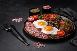 Tasty breakfast consists of eggs, bacon, beans, tomatoes, with spices and herbs photo