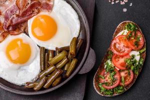 Tasty breakfast consists of eggs, bacon, beans, tomatoes, with spices and herbs photo