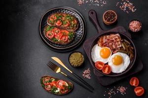 Tasty breakfast consists of eggs, bacon, beans, tomatoes, with spices and herbs photo