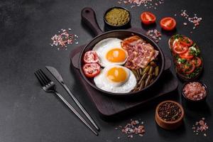 Tasty breakfast consists of eggs, bacon, beans, tomatoes, with spices and herbs photo