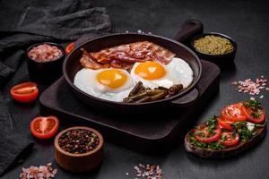 Tasty breakfast consists of eggs, bacon, beans, tomatoes, with spices and herbs photo