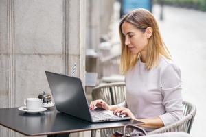 Focused female remote worker using laptop on cafe terrace photo