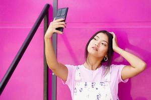 Asian woman taking selfie against pink wall photo