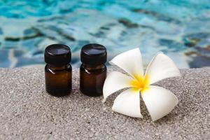 Two bottles of aroma essential oil and flower of frangipani on the swimming pool background for spa theme. photo