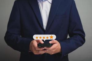 close up on customer man hand pressing on smartphone screen with gold five star rating feedback icon and press level excellent rank for giving best score point to review the service , business concept photo