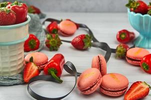 Strawberry macarons of pink color with strawberries and peppers on light wooden background