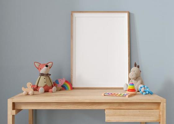 Empty vertical picture frame standing on the desk in modern child room. Frame mock up in contemporary style. Free, copy space for picture, poster. Plush and wooden toys. Close up view. 3D rendering.