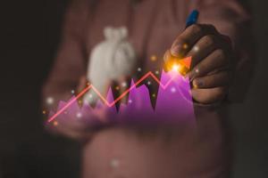 Closeup shot of business man is holding a money bag and pen write to the virtual stock graph photo