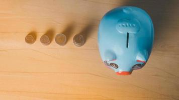 Top view of blue piggy bank and coin orange light on the wooden table background photo