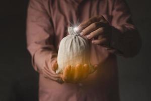 El primer plano de un hombre de negocios sostiene una bolsa de dinero en la luz gráfica de la computadora de fondo oscuro y borroso foto