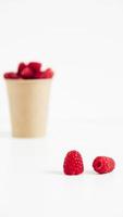 Fresh red raspberries in a paper cup on a white table background photo