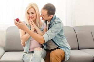 Man surprising his girlfriend with a gift on the couch at home in the living room photo