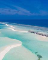 Beautiful drone photo with a wooden water villas and wonderful blue lagoon crystal clear water with sandbank and endless blue sky. Amazing aerial landscape, island paradise , summer vacation concept