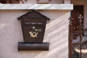 acero antiguo, buzón de correo de hierro en una pared de ladrillos de piedra, junto a una valla de madera en el edificio o en la puerta de la casa. objeto relacionado con el hogar, buzón de correo foto