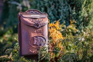 Mailbox or letterbox. Beautiful vintage mailbox on a natural stand, bushes around. Iron mailbox photo