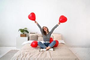 día de San Valentín. joven mujer feliz en la cama con globos en forma de corazón rojo foto