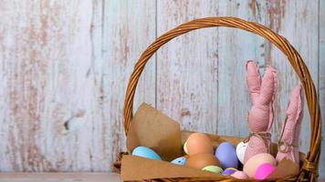 primer plano de conejitos de juguete rosa en la cesta llena de huevos coloridos. feliz pancarta de pascua con lugar para texto foto