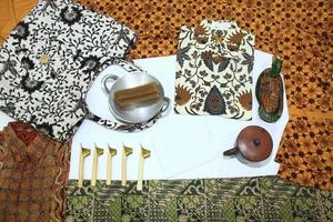 flat lay batik clotes with canting, small pan and wax earthenware glass isolated on white background