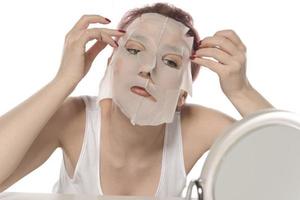 Face care and beauty treatments. Woman with a sheet moisturizing mask on her face isolated on white background photo