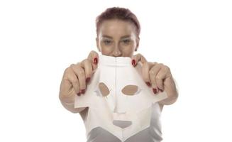 Face care and beauty treatments. Woman with a sheet moisturizing mask on her face isolated on white background photo