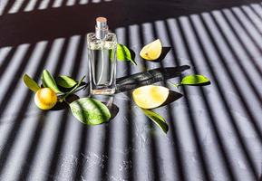 an open bottle of women's perfume stands on a dark background among a ripe tangerine and sunny shadows . presentation and advertising of the product. photo