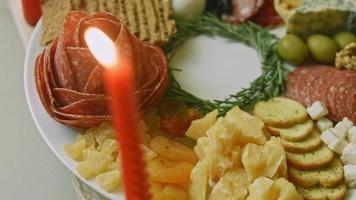 Flat charcuterie with salami, different kinds of cheese. It has dried fruits, various nuts and honey. Holiday arrangement with burning candles