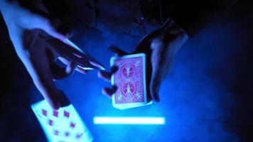primer plano, manos de un mago que realiza trucos con una baraja de cartas. iluminación azul. el prestidigitador muestra el enfoque. persona irreconocible. video