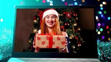 Beautiful woman laughs and congratulates relatives on Christmas via laptop online. View from web camera against background Christmas tree. Remote communication due to coronavirus and quarantine video