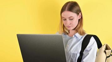 närbild av en kvinna studerande skriver på bärbar dator mot gul bakgrund.studio porträtt.tillbaka till skola video