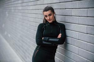 Young sportive girl in black sportswear outdoors near gray wall photo