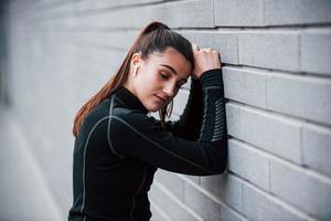 Young sportive girl in black sportswear outdoors near gray wall photo