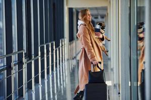 Young female passenger in warm clothes walking with her dog in airport hall photo