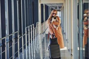 Young female passenger in warm clothes walking with her dog in airport hall photo