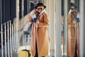 joven pasajera vestida con ropa de abrigo con billetes y equipaje en la sala del aeropuerto foto