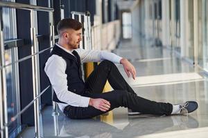 Young male passenger in elegant formal clothes sitting in the airport hall photo