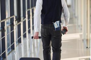 Rear view of male passenger in elegant formal clothes is in the airport hall with tickets in his pocket photo