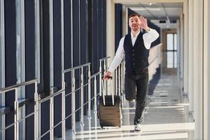 Man in formal clothes and with baggage is running forward and busy for a plane photo