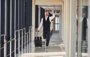 Man in formal clothes and with baggage is running forward and busy for a plane photo